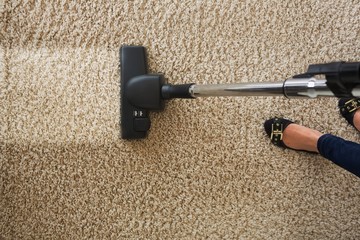 Cropped image of woman cleaning carpet with vacuum cleaner
